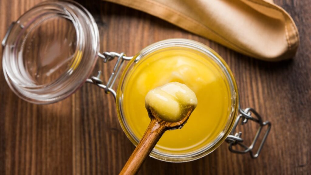 A jar of golden clarified butter (ghee) with a spoon, ideal for supporting muscle and  weight gain