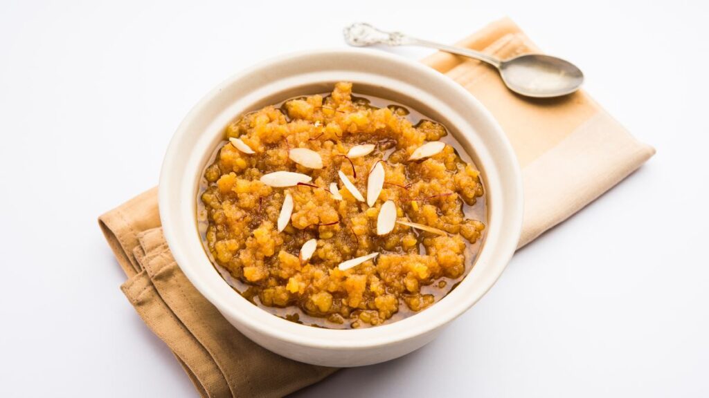 Image of halwa in a bowl with a spoon beside it, placed on a kitchen cloth.