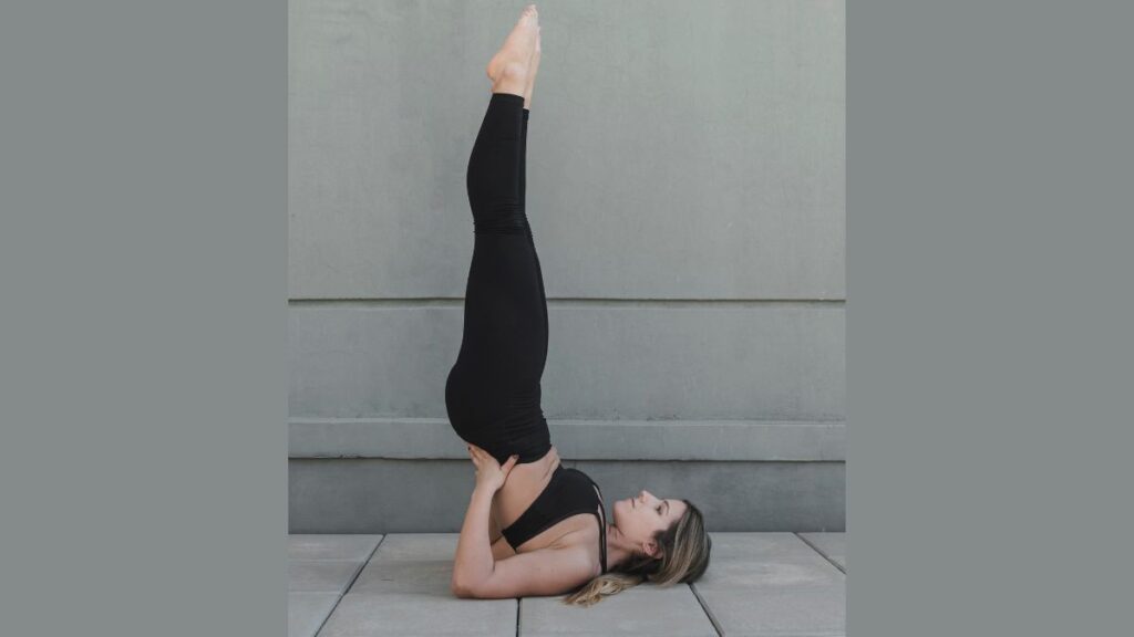 One woman performing Shoulder Stand Pose (Sarvangasana) on a yoga mat, a beneficial yoga pose for skin health and acne relief.